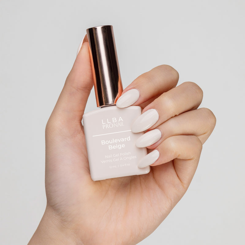 Hand with beige nails holding LLBA ProNail Boulevard Beige nail gel polish, set against a white background.