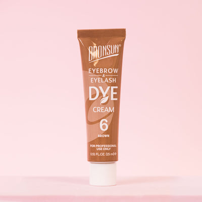 Brown eyebrow and eyelash dye cream tube displayed on a pink background