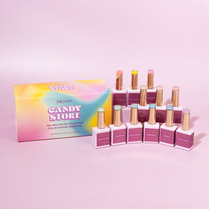 A collection of nail polish bottles with gold caps arranged beside a colorful "Candy Store" box on a pastel pink background.