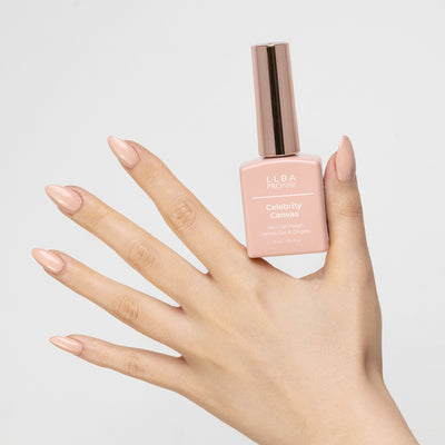 Hand holding a bottle of LLBA Pronail Celebrity Canvas Nail Gel Polish, featuring a nude beige color, with a matching nail color on the hand, against a white background.