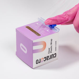 Gloved hand using the cutter on Curacoro clear plastic wrap packaging, 42mm x 200m, for brow lamination.