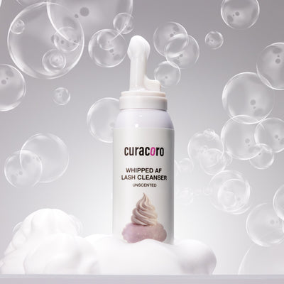 curacoro whipped AF lash cleanser bottle with bubbles and foam on a gray background