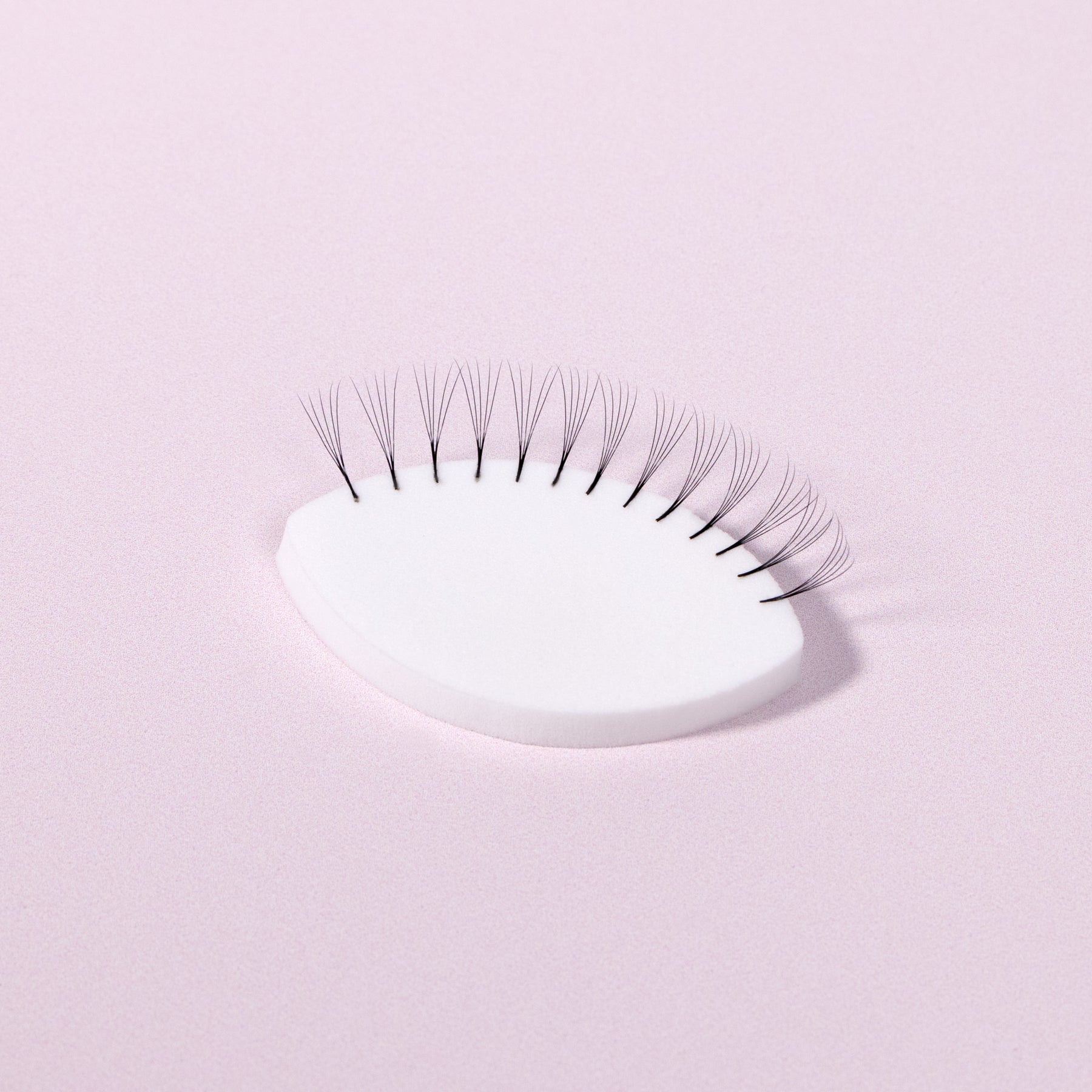 A White Lash Practice Sponge over a light pink background. 