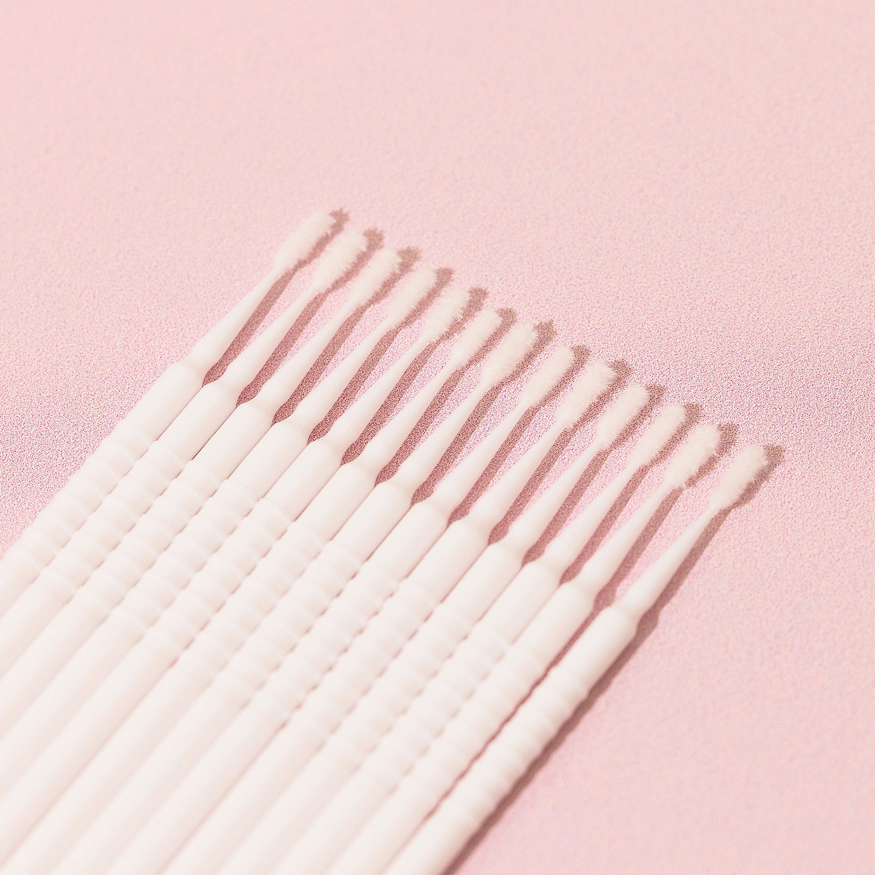 13 white Disposable Micro Applicators over a pink background. 