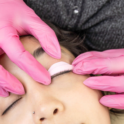 Lash tech using pink gloves applying lash rods on client's eyes.