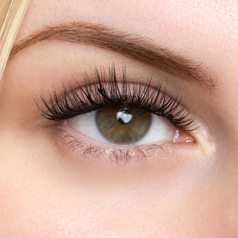 Close-up of an eye showcasing long, voluminous lashes with a natural, soft curl effect, highlighting the application of lash extensions for a fuller look.