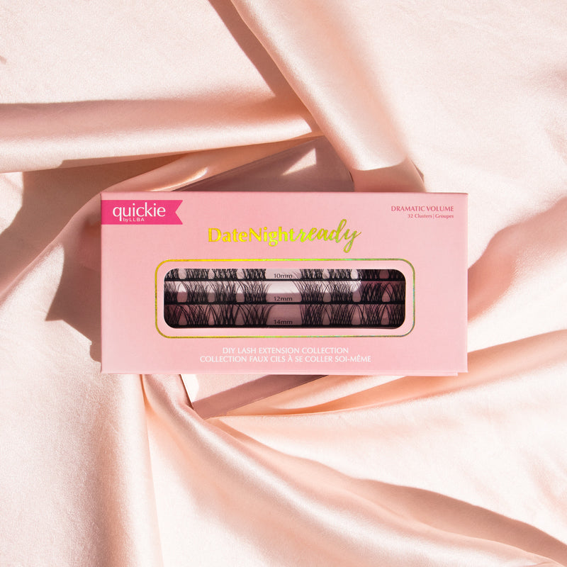 Pink lash extension kit box with transparent window showing three rows of lash clusters in different lengths, placed on soft, peach-colored fabric.