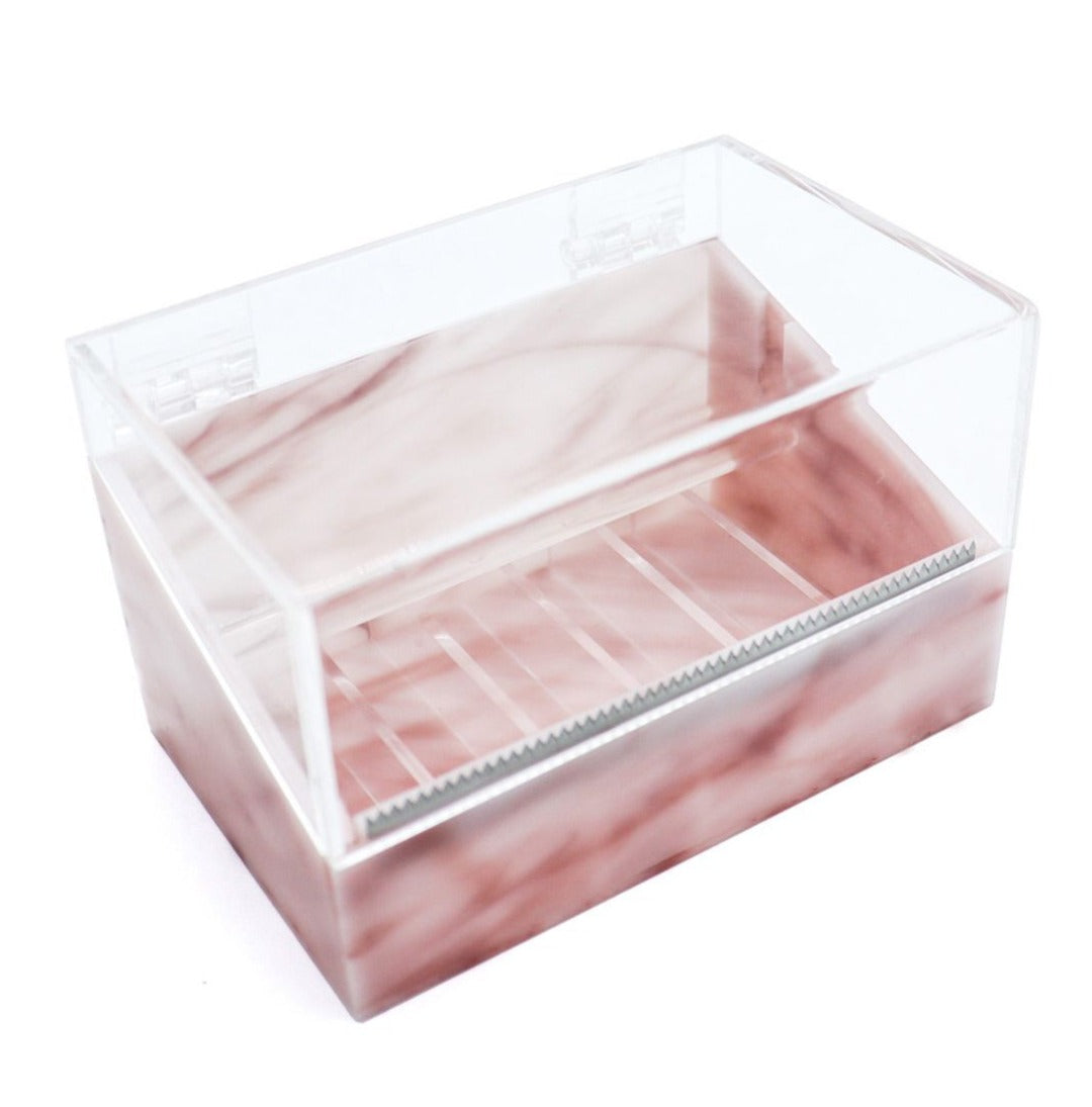 Pink marble acrylic tape dispenser with a clear hinged lid, built-in serrated cutter, and multiple slots for organizing tape rolls.