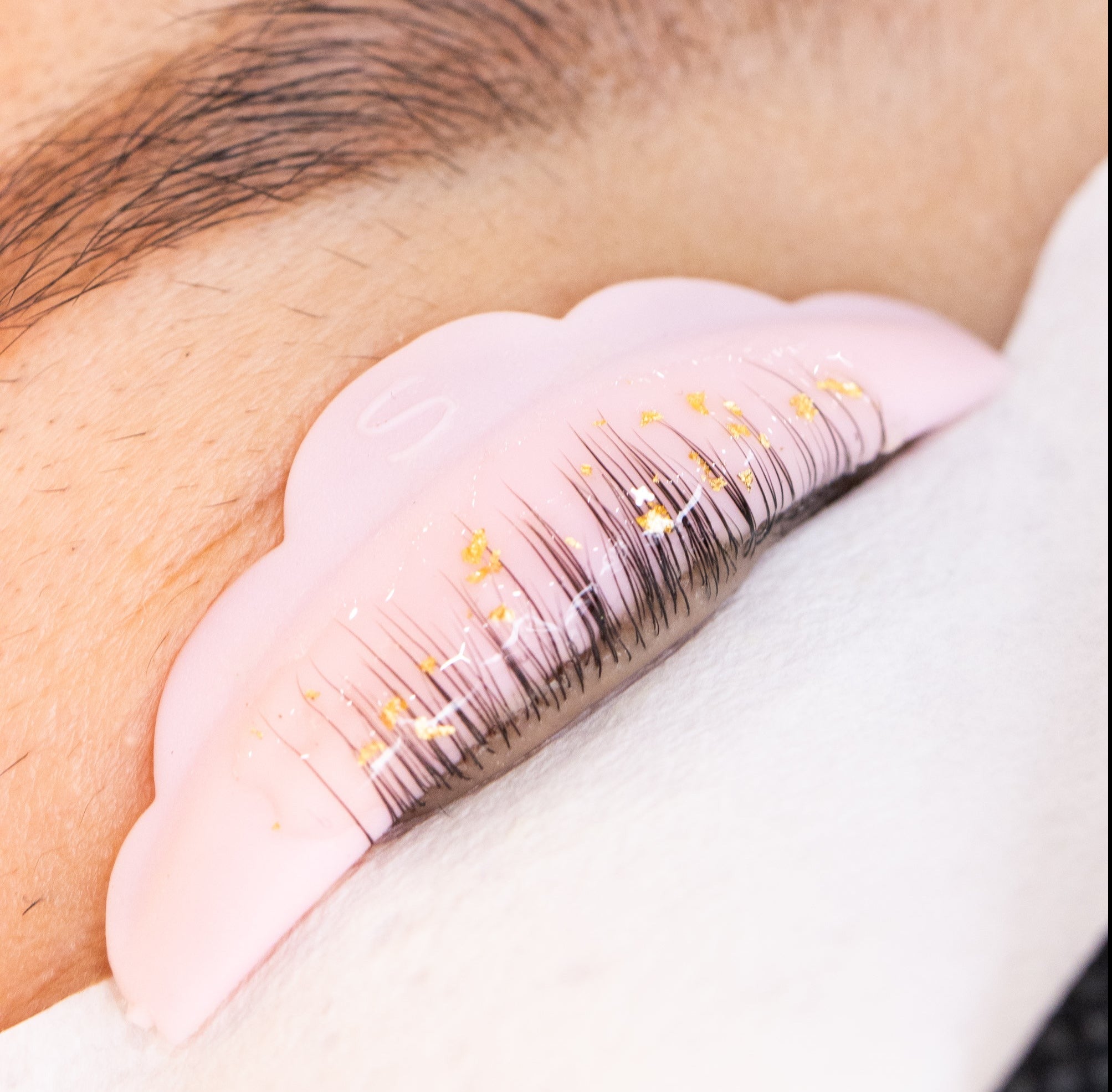 Close-up of eyelashes with gold accents on a pink silicone pad, resting on a white surface.