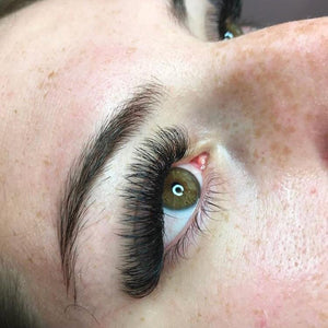 Close-up of a green eye with full, voluminous eyelash extensions, showcasing professional lash application.